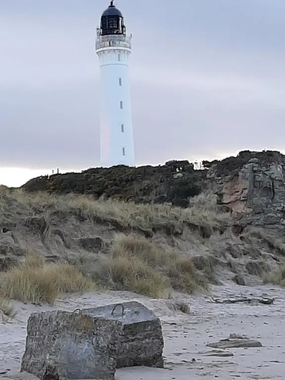 a lighthouse sitting on top of a rocky hill at Taid's Retreat Silversands Cove beach lossiemouth in Lossiemouth