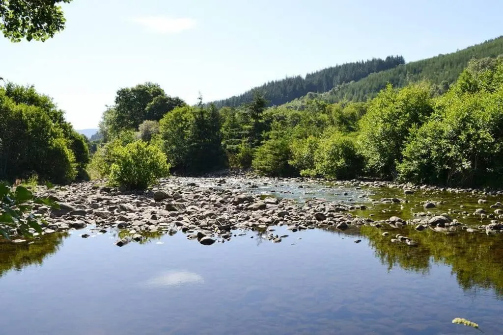 a river with a bunch of rocks and trees at Herons Rest in Drumnadrochit
