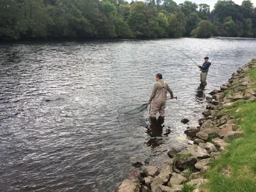 two men are standing in the water fishing at Highland HotTub Retreat, on NC500 in Inverness