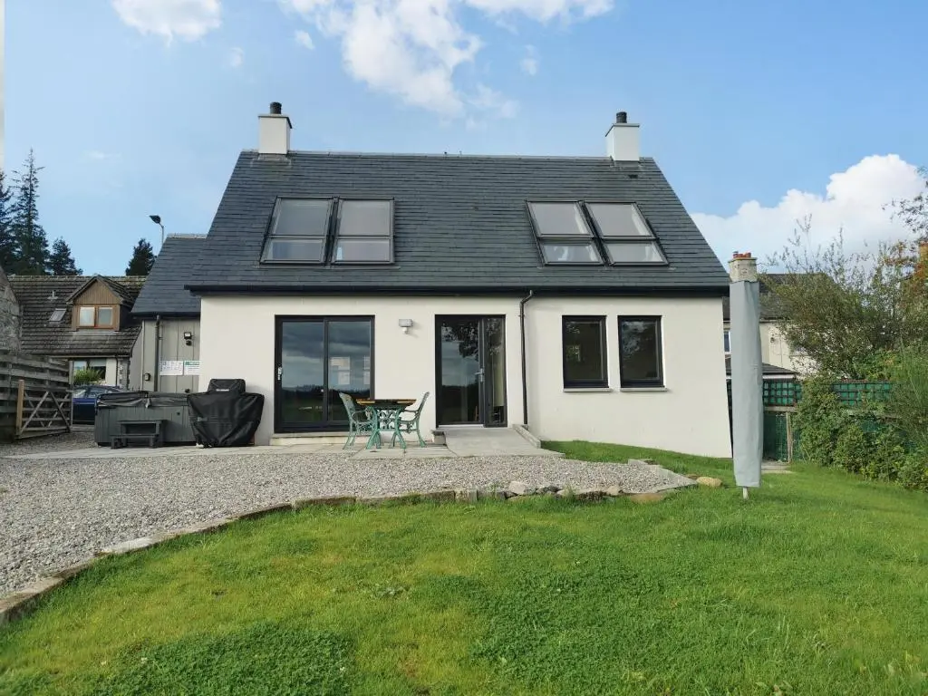 a white house with a table and chairs in the yard at Berg Cottage in Ballindalloch