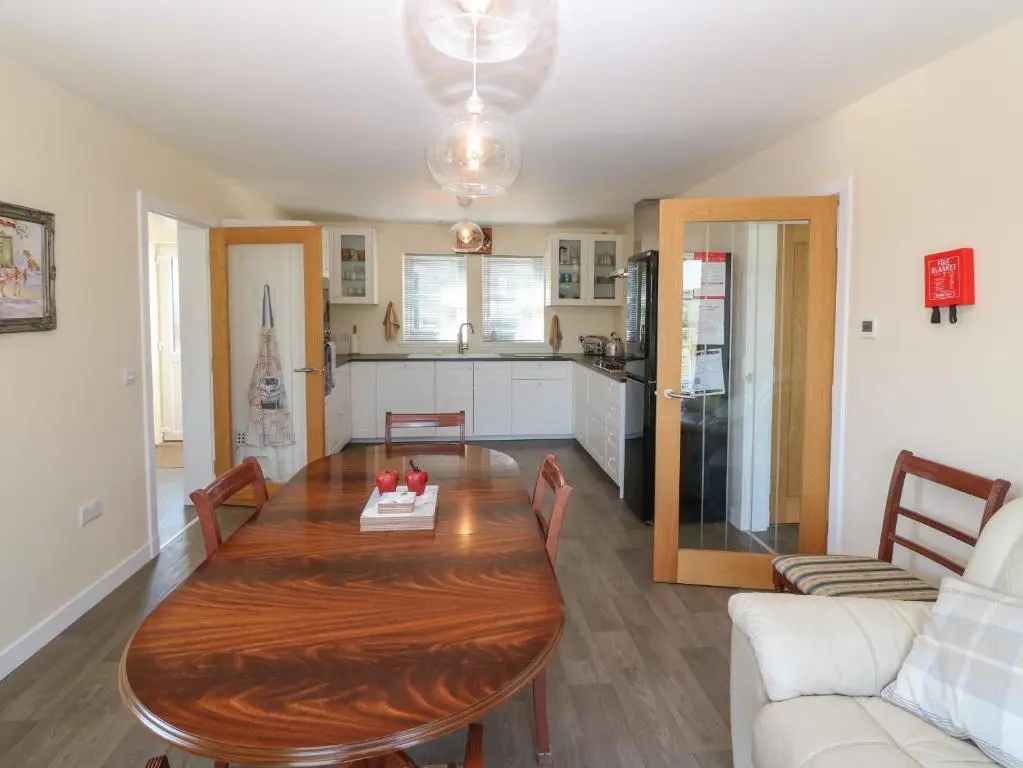 a living room with a wooden table and a kitchen at Berg Cottage in Ballindalloch