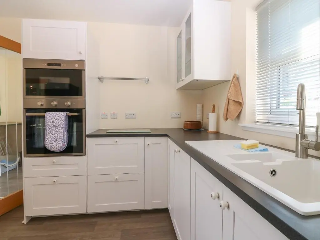 a kitchen with white cabinets and a sink at Berg Cottage in Ballindalloch