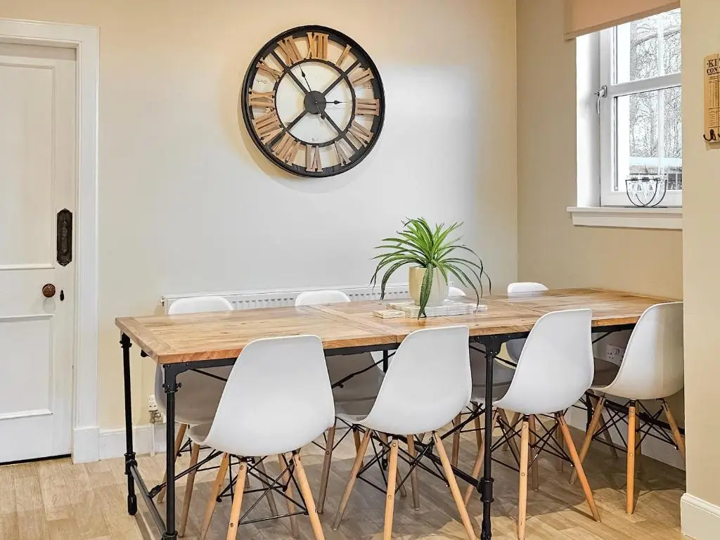 a dining room table with white chairs and a clock on the wall at Balmore Farmhouse in Lochend