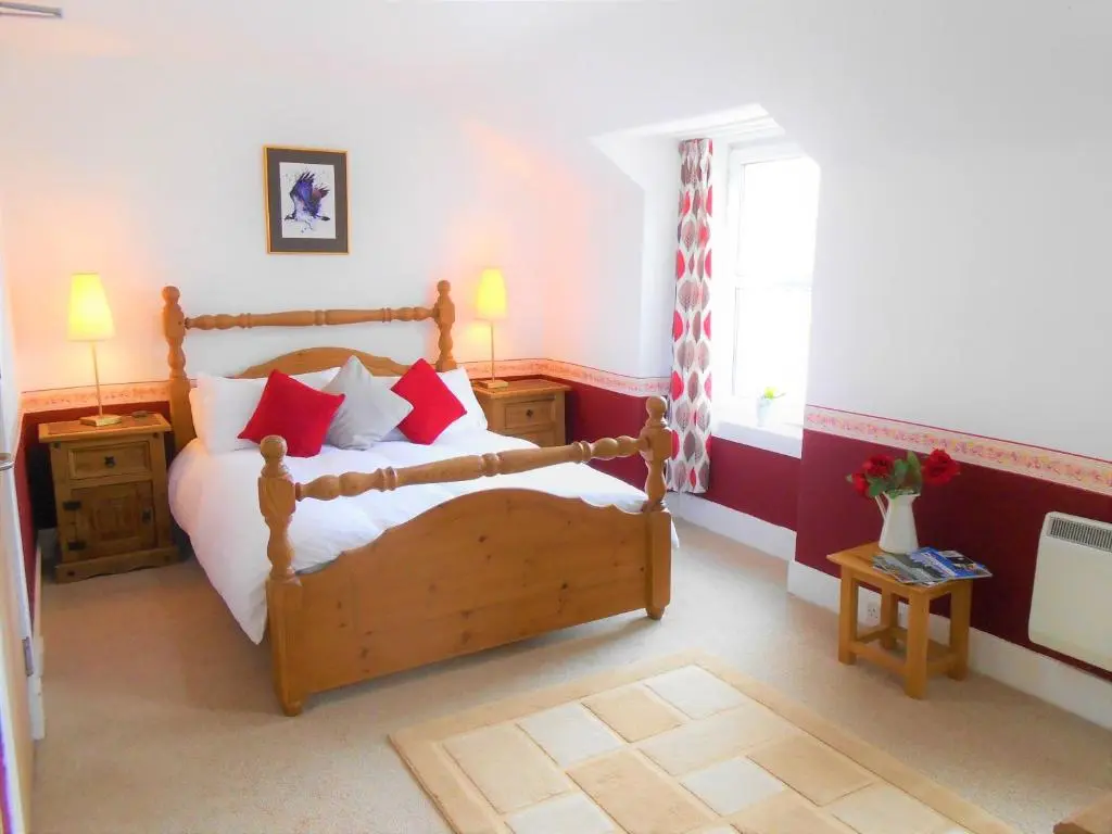 a bedroom with a wooden bed with red pillows at The Osprey Hotel in Kingussie