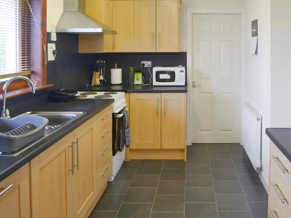 a kitchen with wooden cabinets and a sink at Cluaran Cottage in Tain