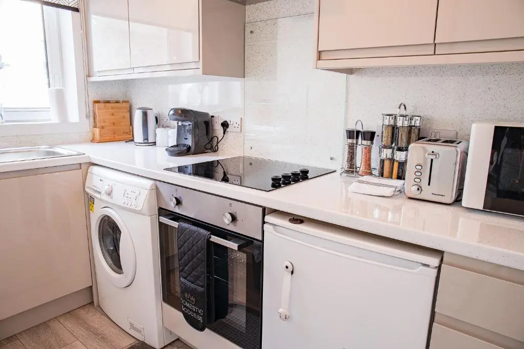 a white kitchen with a stove and a dishwasher at Millburn Apartment in Inverness
