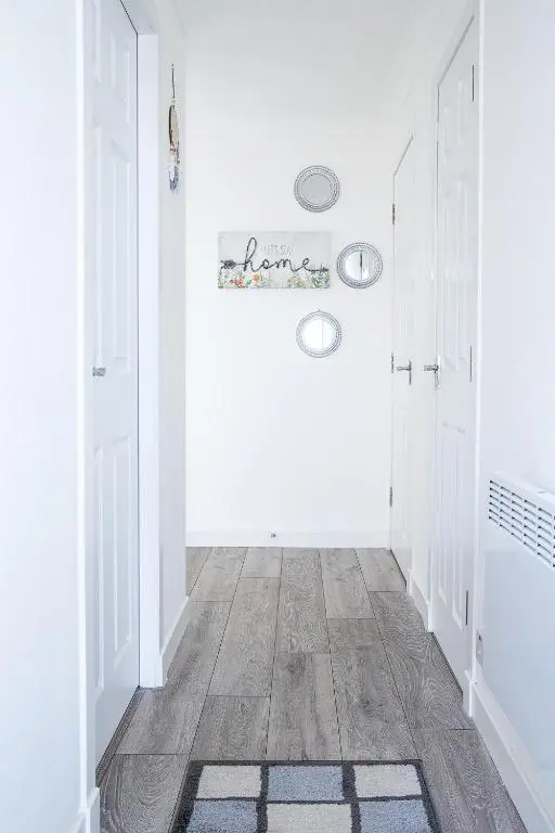 a hallway with white walls and wooden floors and white doors at Millburn Apartment in Inverness