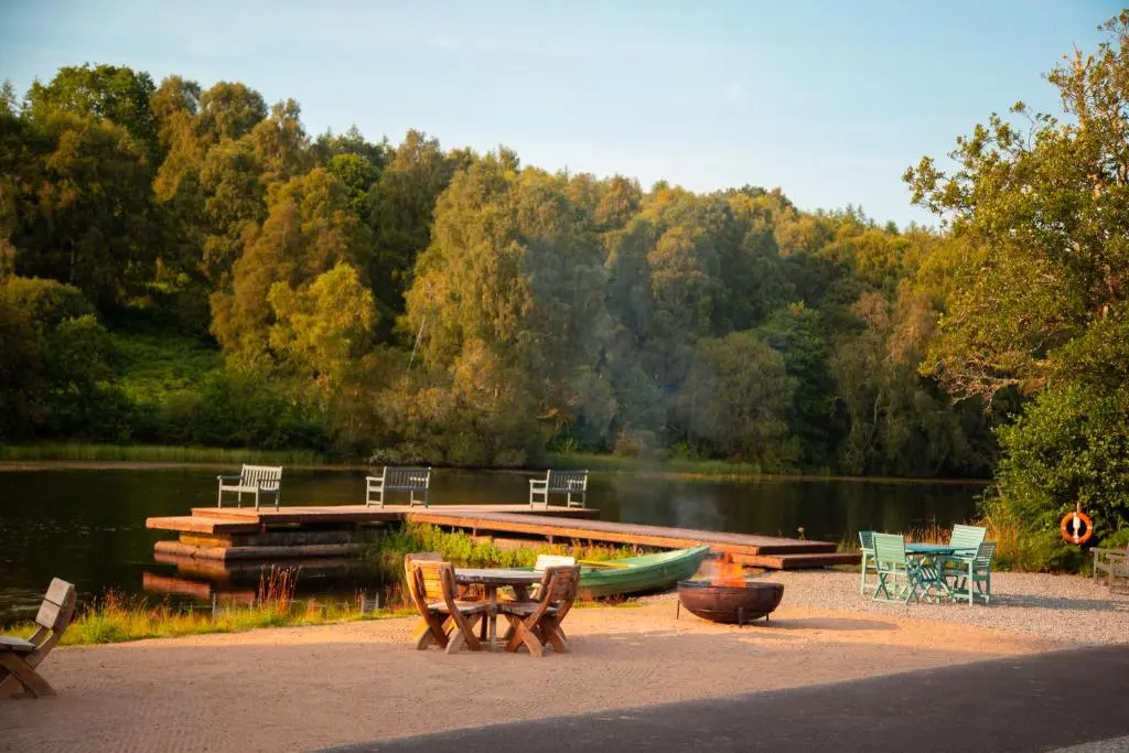 a picnic table and chairs next to a dock with a boat at Balnagown Estates Peat Cottage in Kildary
