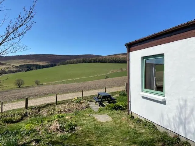 a building with a picnic table next to a field at Easter Corrie Cottages in Ballindalloch