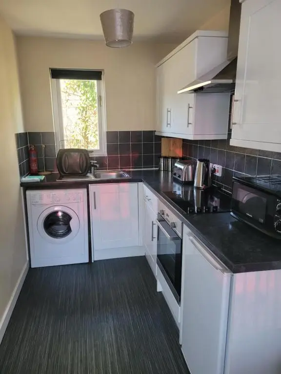 a kitchen with white cabinets and a washing machine at Arisaig Flat in Inverness
