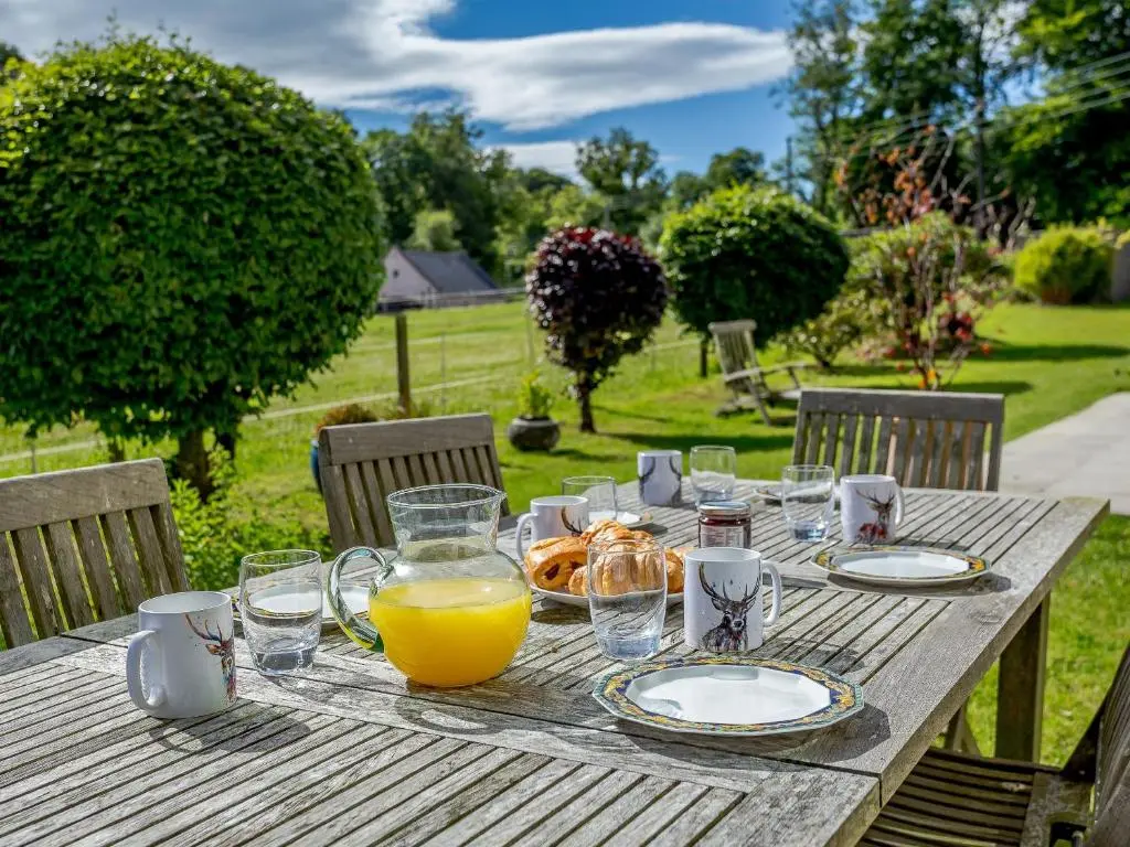 a wooden table with a plate of food and orange juice at Skene House Court in Dunecht