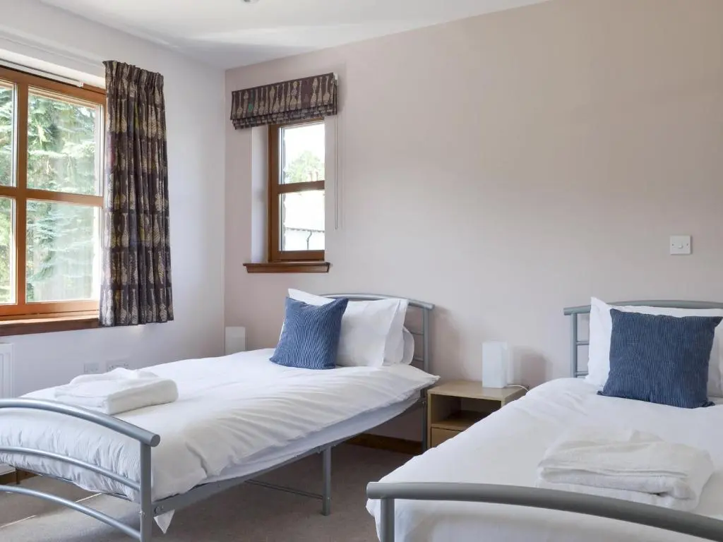 two beds in a room with two windows at Battanropie Lodge in Carrbridge