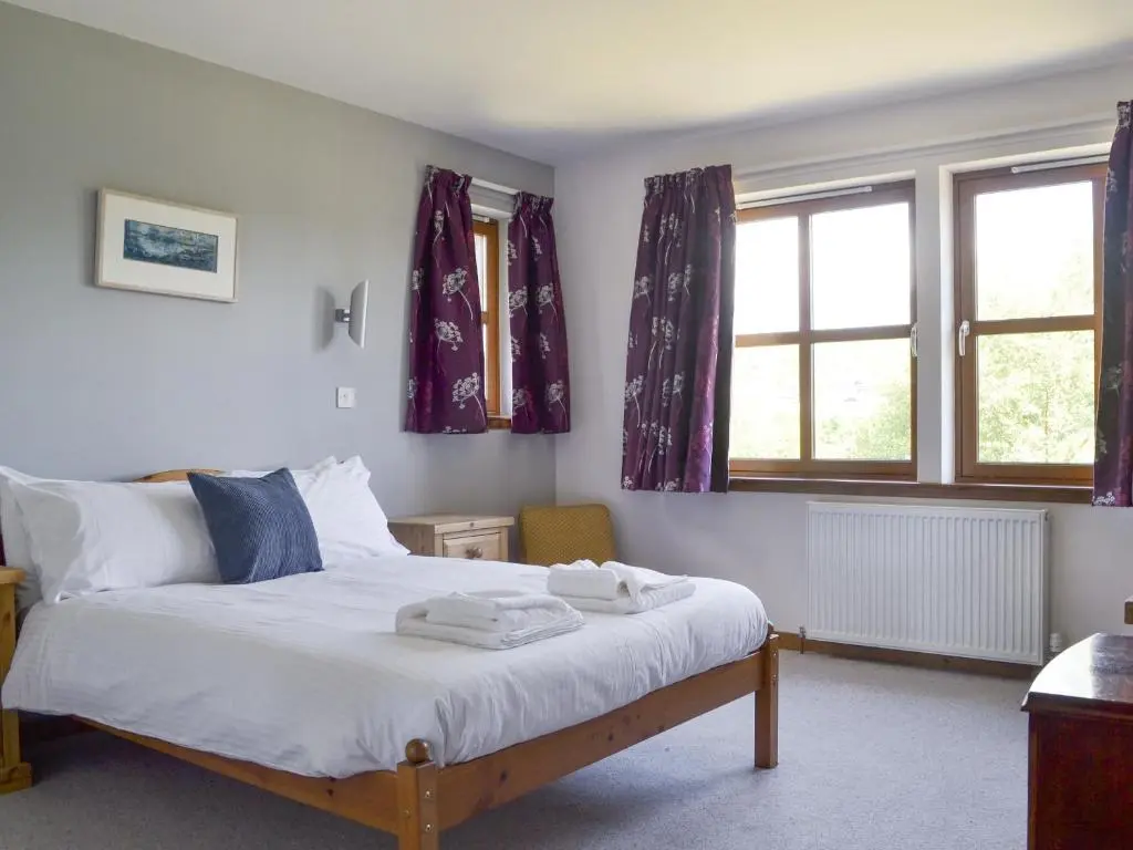 a bedroom with a bed and two windows at Battanropie Lodge in Carrbridge
