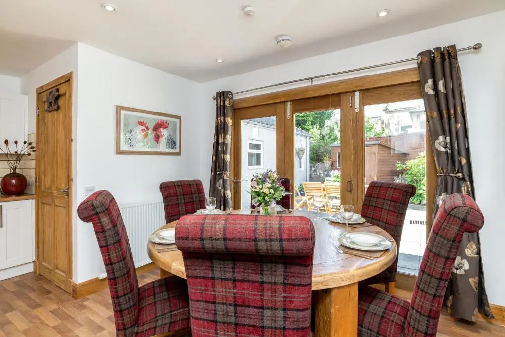 a dining room with a wooden table and chairs at Dormie Cottage, lovely bright and spacious bungalow with wood fire in Ballater