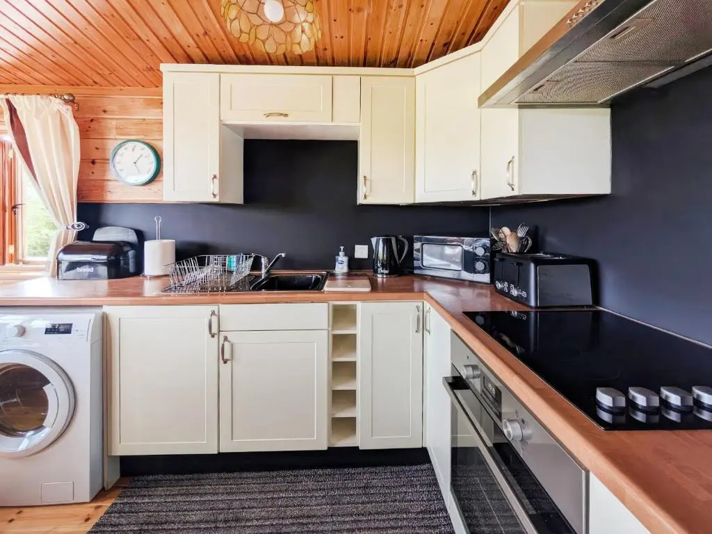 a kitchen with white cabinets and a washer and dryer at Red Kite Cottage in Tore