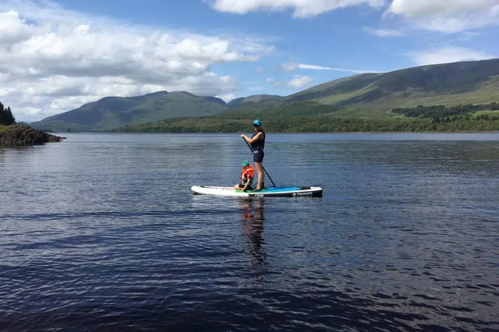 a man standing on a paddle board on a lake at The Snug at the Ski Lodge, Aviemore in Aviemore