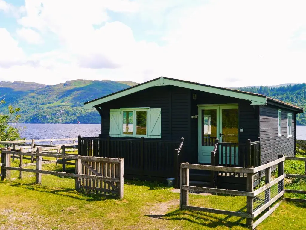 a black house with a fence in front of a lake at Cabins at Old Pier House in Fort Augustus