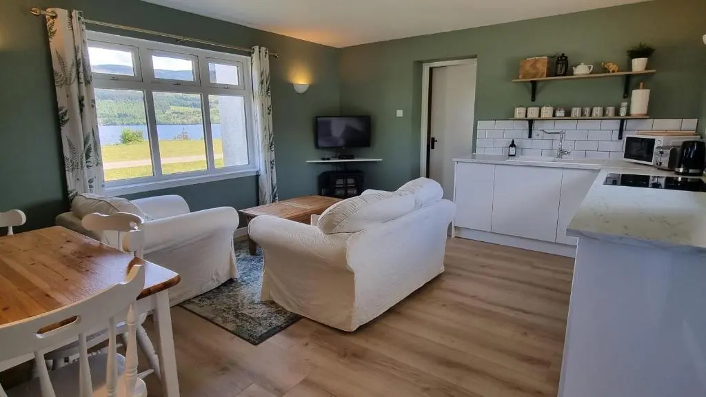 a living room with white furniture and a kitchen at The Apartment at Old Pier House in Fort Augustus