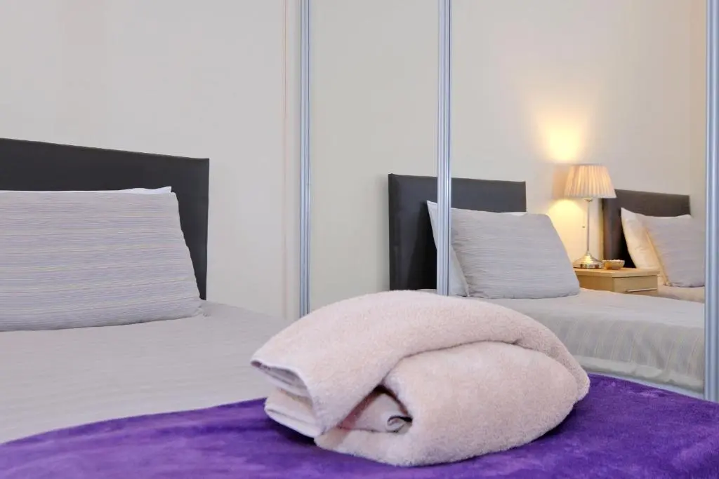 a white bed with a towel on a purple rug at Caledonia Newhills Apartment in Aberdeen