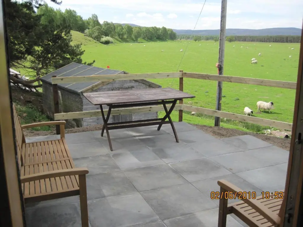 a patio with a table and chairs and a field of sheep at Glenfeshie Hostel in Insh