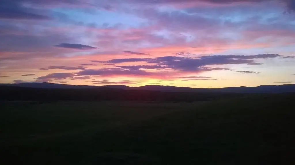 a sunset over a field with mountains in the background at Glenfeshie Hostel in Insh