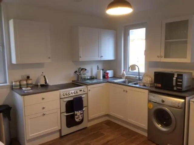 a kitchen with white cabinets and a stove top oven at Centrally located 2 bed modern flat with harbour views in Wick