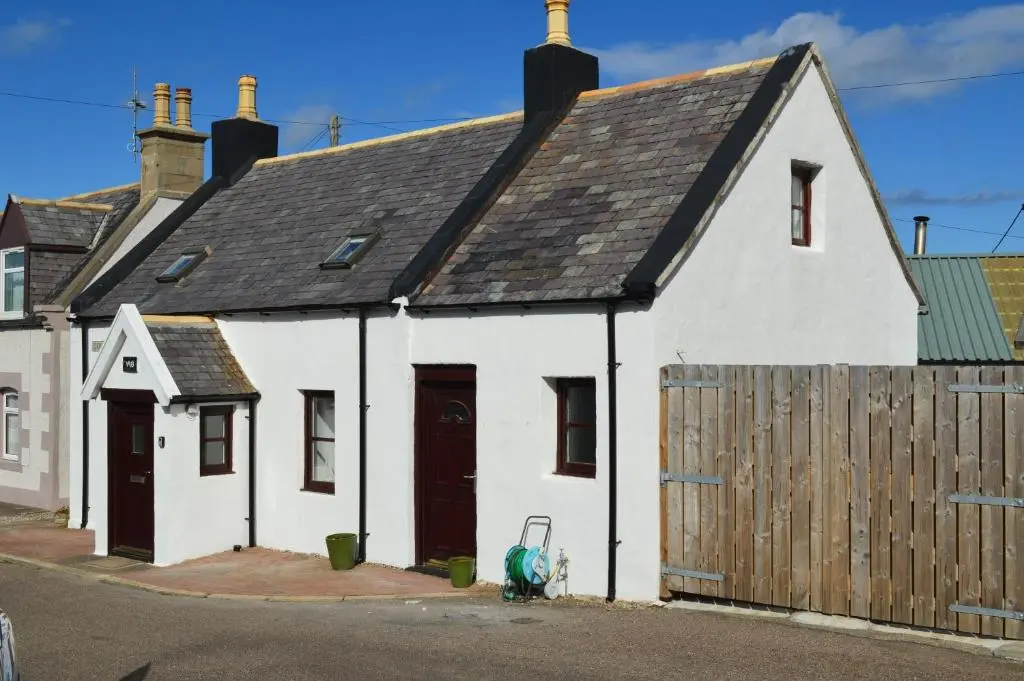 a small white house with a wooden fence at 4-Bed Cottage in Portknockie Near Cullen Moray in Portknockie