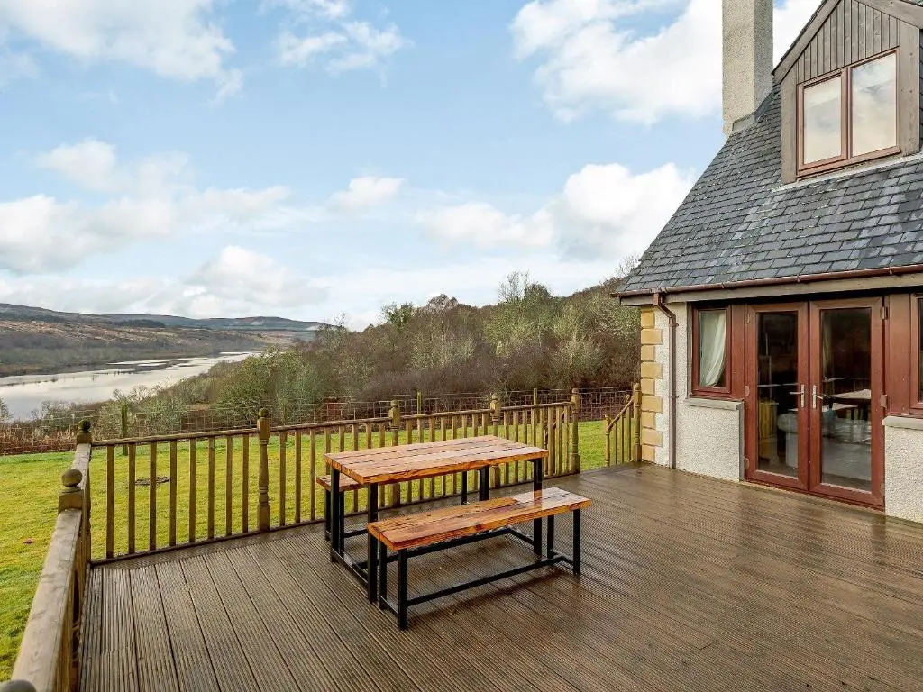 a wooden deck with a table and a bench on it at The Big Hoose in Achnahanat