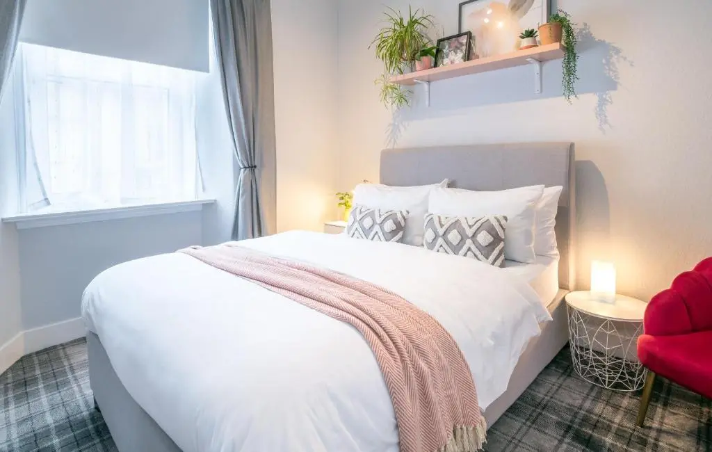 a bedroom with a white bed and a red chair at Macdonald Street Snug in Inverness