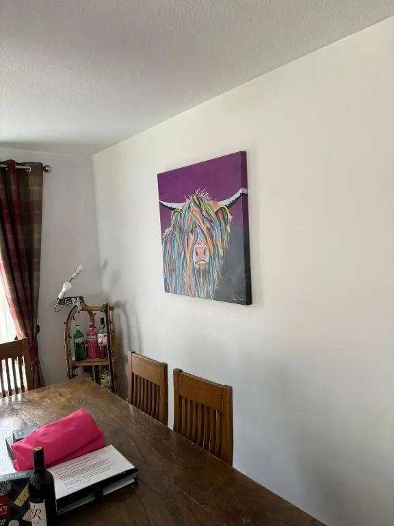 a dining room table with a painting on the wall at Cairngorm Cottage in Aviemore