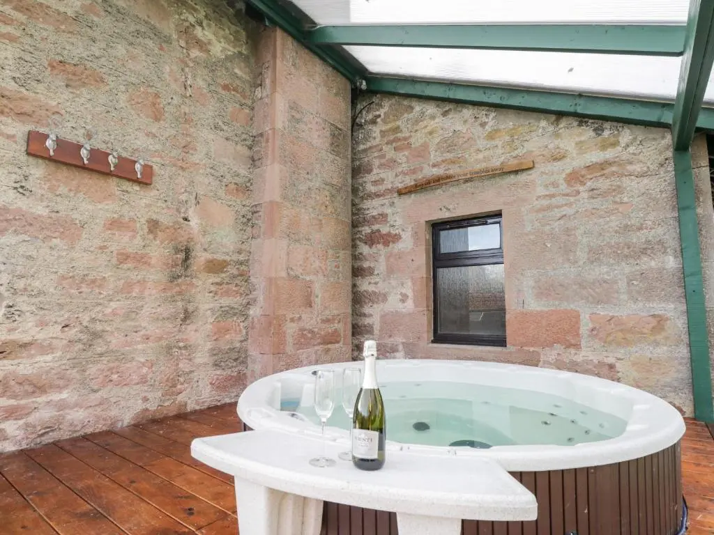 a bath tub with a bottle of wine on a table at Orrinside in Muir of Ord