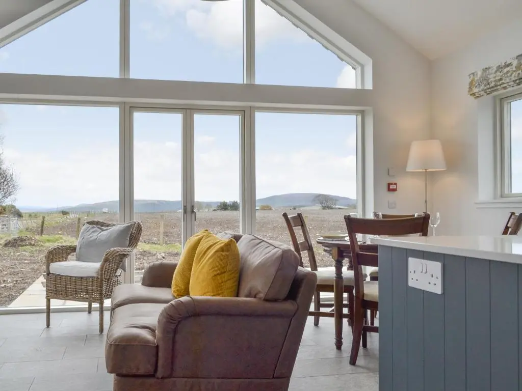 a living room with a table and chairs and windows at Muirtown Lodge in Keith