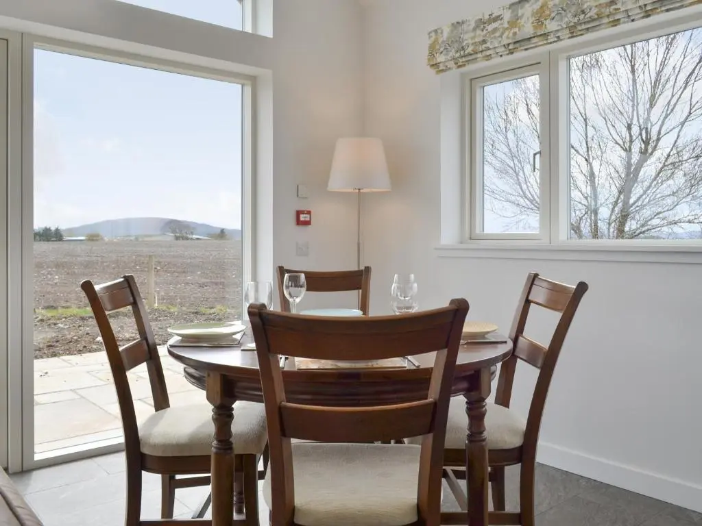 a dining room with a table and chairs and windows at Muirtown Lodge in Keith
