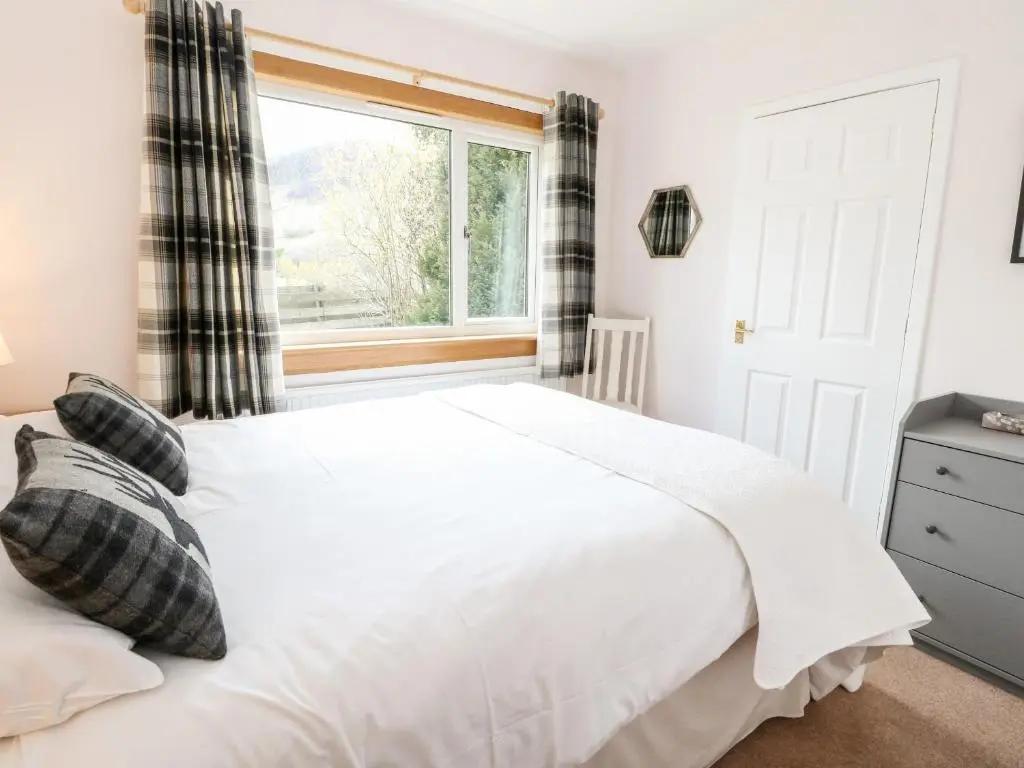 a bedroom with a white bed and a window at Beechwood Cottage in Pitlochry