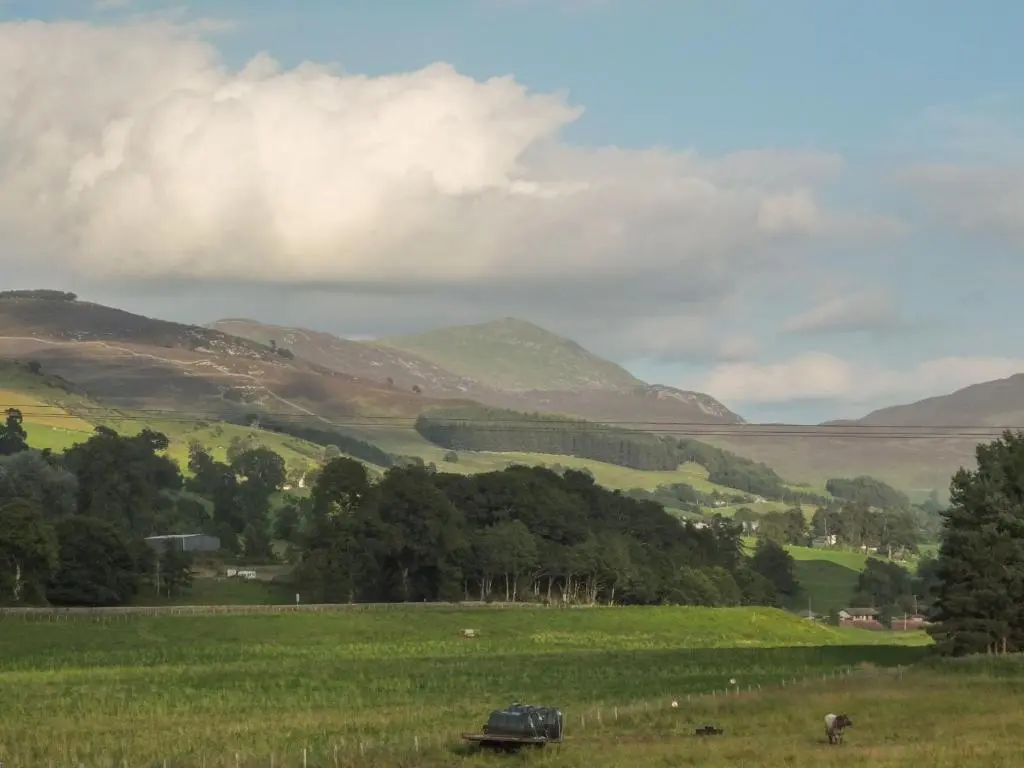 a car in a field with mountains in the background at Beechwood Cottage in Pitlochry
