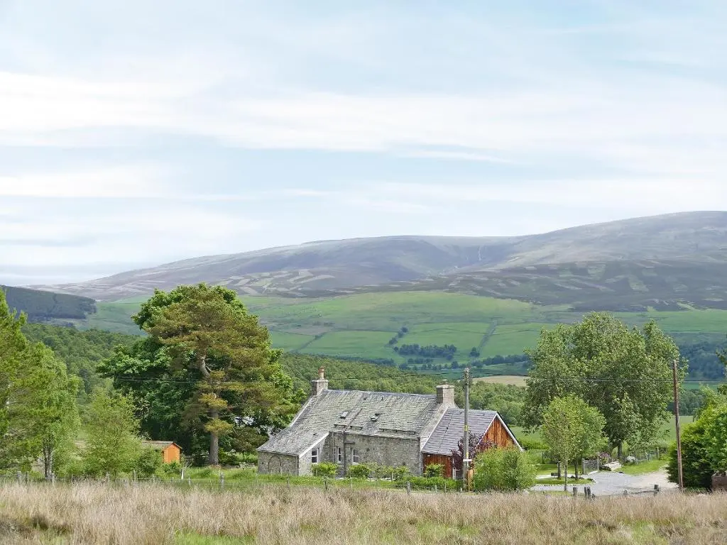 an old house in a field with hills in the background at Easter Lettoch in Advie