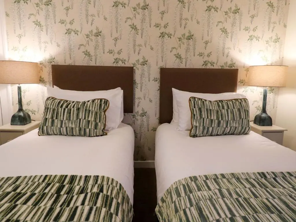 two beds in a bedroom with two lamps and wallpaper at Paye House - Cromarty in Cromarty