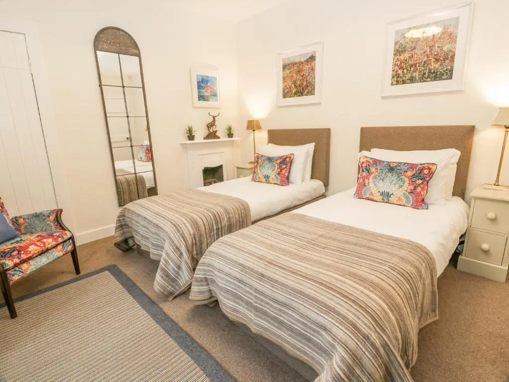a bedroom with two beds and a chair and a mirror at Beechgrove Cottage - Pitmedden Gardens in Ellon