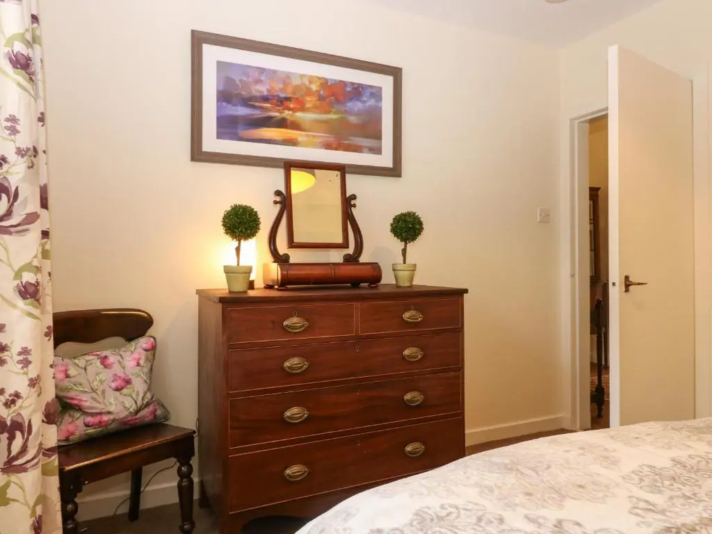 a bedroom with a dresser with a mirror and a chair at Steading Cottage - Craigievar Castle in Alford