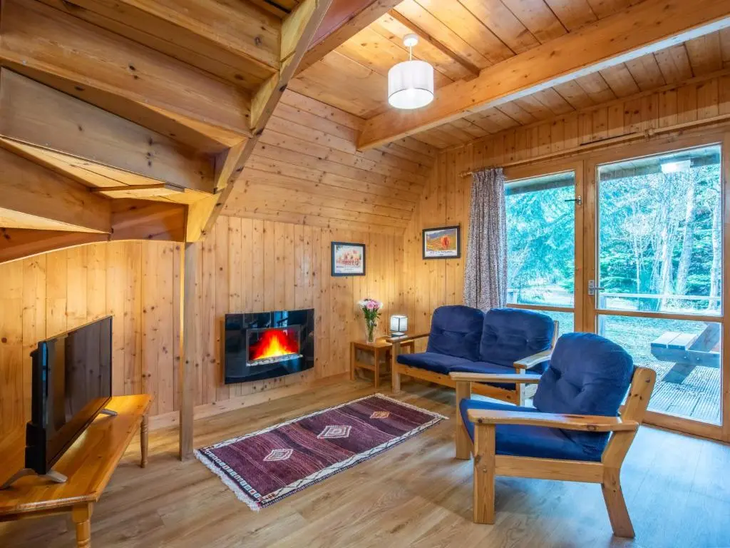 a living room with a fireplace in a log cabin at Chalet Rowan Cottage by Interhome in Inverness