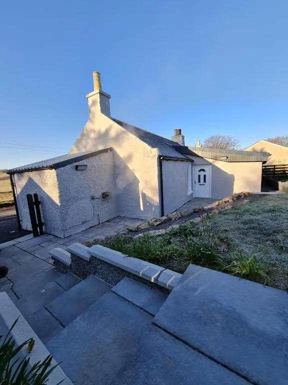 a small white house sitting on top of a yard at Bruxie Holiday Cottages - Honeysuckle Cottage in Maud