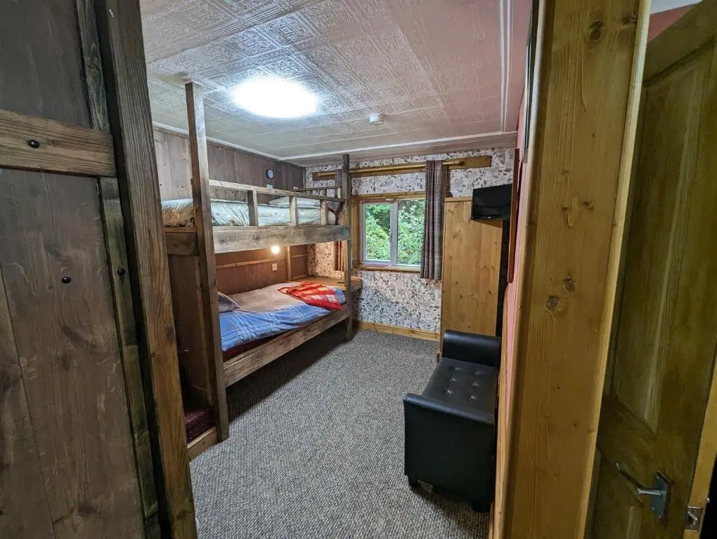 a small room with bunk beds and a chair at The Steading Highland Glen Lodge in Drumnadrochit