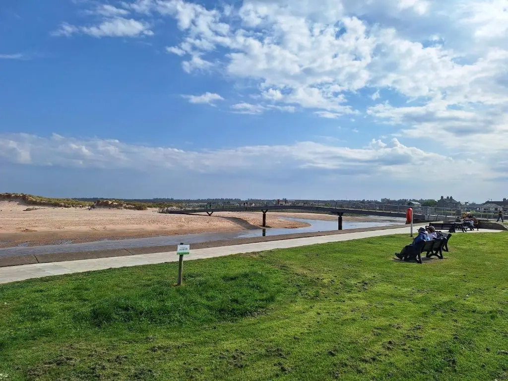 a group of people sitting in the grass near the beach at 1 Fulmar Road**Next to West Beach and Golf Course in Lossiemouth