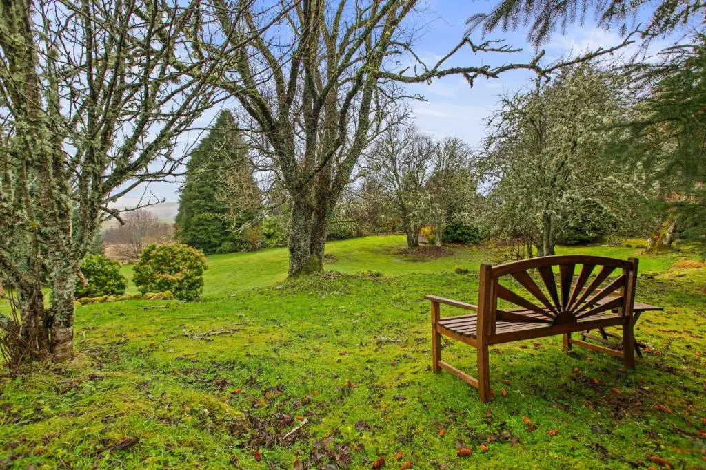 a wooden bench sitting in a park with trees at Freuchies Mill - A Holiday Home For All Seasons. in Blairgowrie