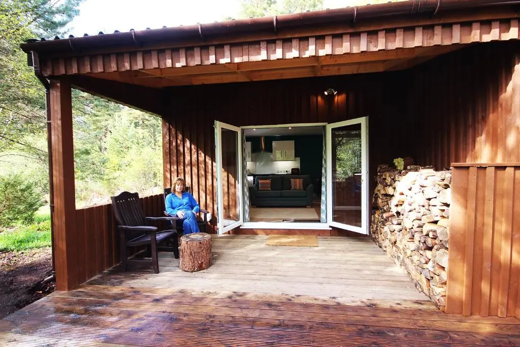 a woman sitting on the porch of a cabin at The Cabin at Easter Arr in Auldearn