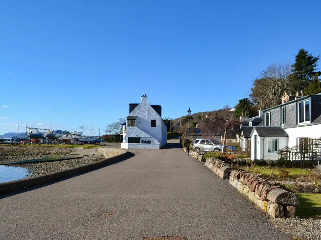 a road leading to a white house with a church at The Shore in Fortrose