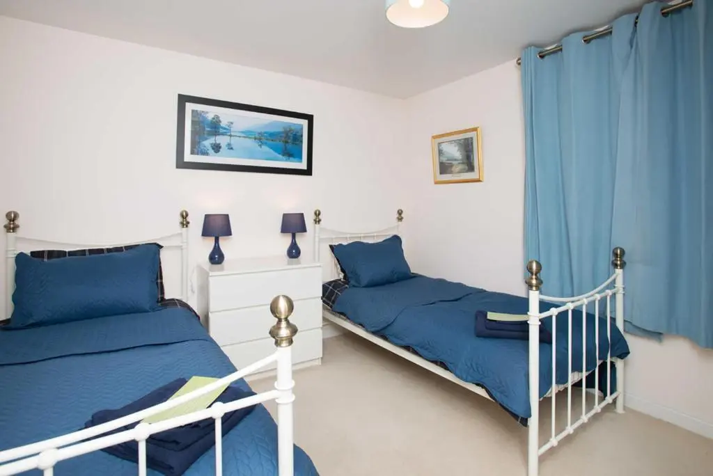 two beds in a bedroom with blue curtains at Lovely 2 bedroom apt in Ballater on the River Dee in Ballater