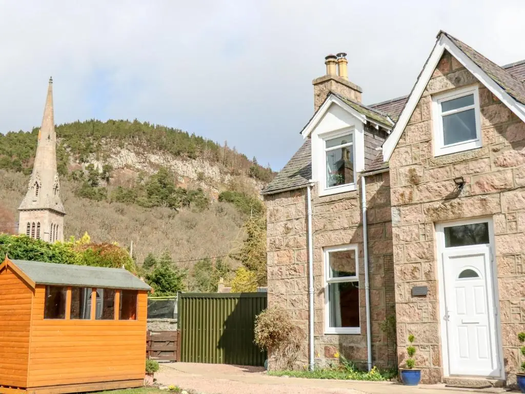 an old stone house with a church in the background at Gairnlea House in Ballater