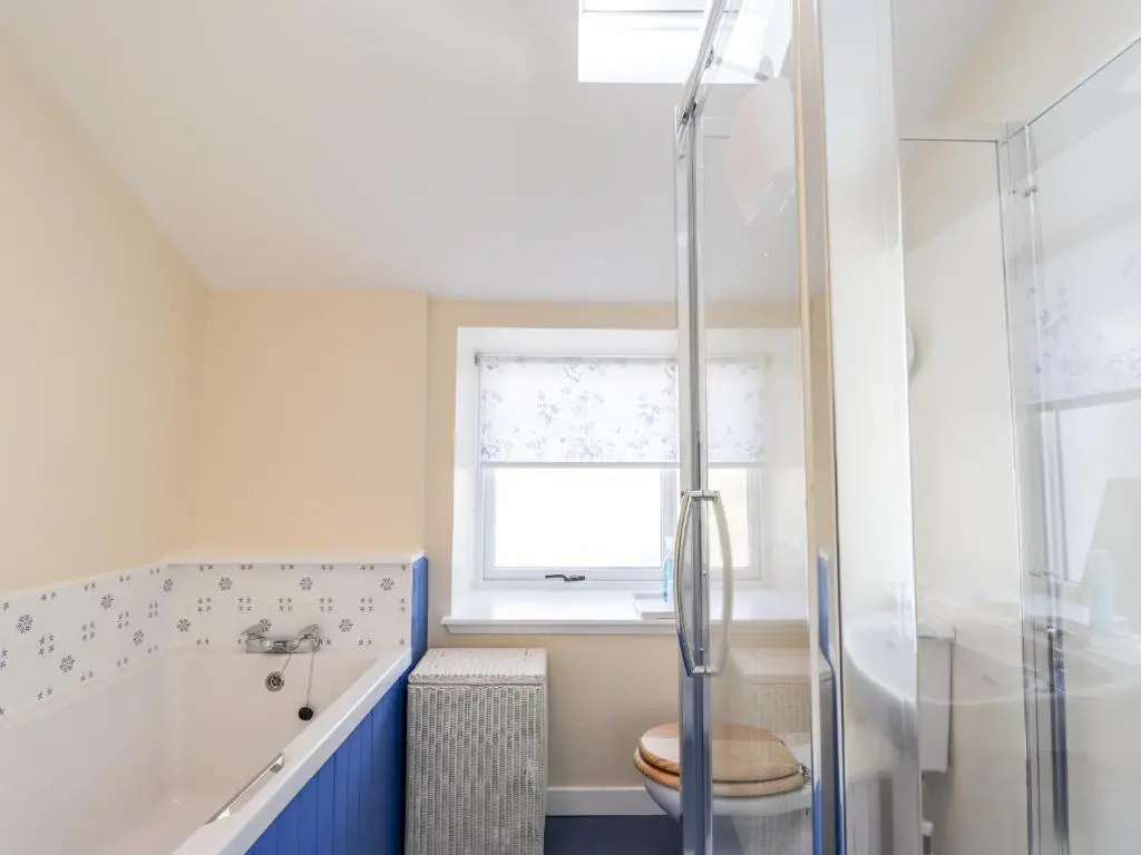 a bathroom with a tub and a toilet and a window at Balnaird Farmhouse in Strathpeffer