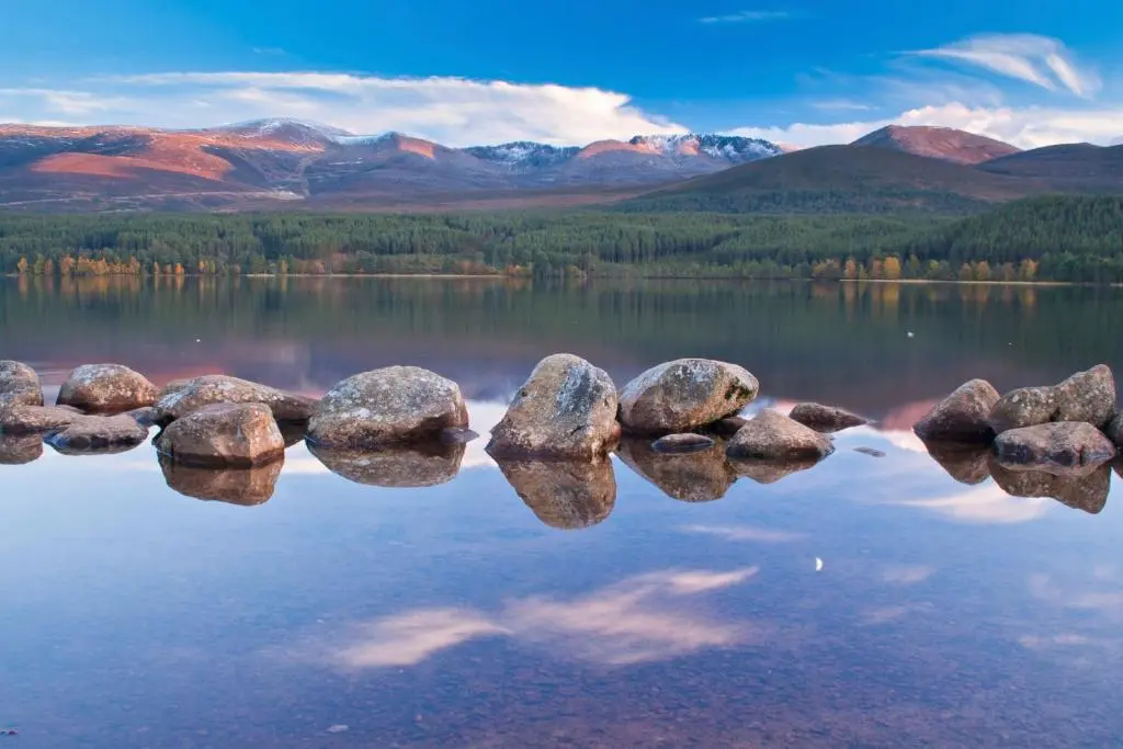 a group of rocks in the water with mountains at Silverglades Holiday Homes in Aviemore